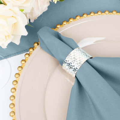 Stylish silver napkin ring on a blue napkin atop a decorative plate.