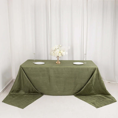 Elegant olive green tablecloth draped over a table with white plates and floral centerpiece.