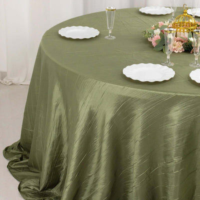 Olive green tablecloth draped on a round table with white plates and floral centerpiece.
