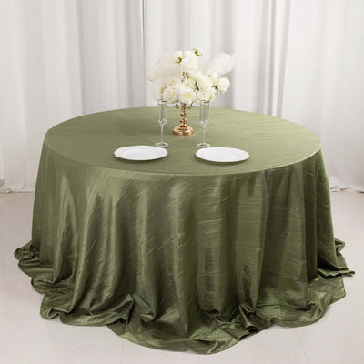 Round olive green tablecloth draped over a table set for dining.