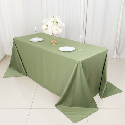 Olive green tablecloth with white plates and floral centerpiece on a dining table.