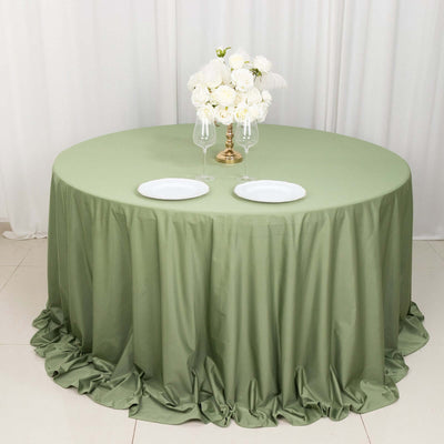 Round olive green tablecloth with ruffled edges, set for dining with plates and flowers.