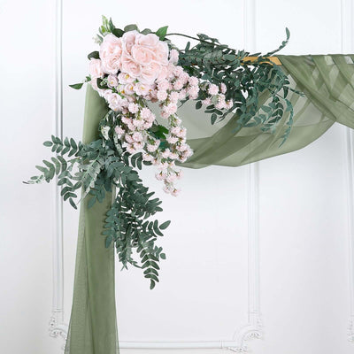 Floral arrangement with pink roses and greenery on a draped fabric backdrop.