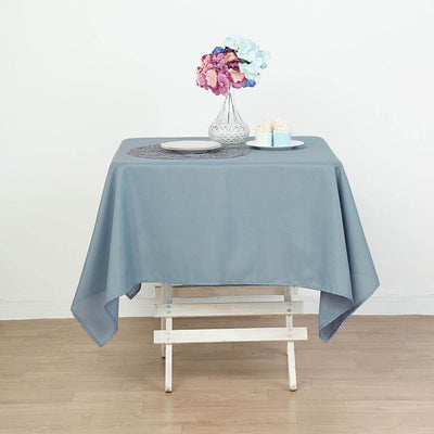 Gray tablecloth draped over a wooden table with flowers and dessert in the background.