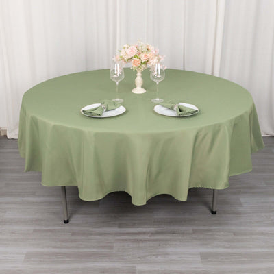 Round olive green tablecloth draped over a table set with plates and glasses.