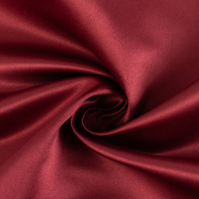 Burgundy satin fabric texture swirled in a circular pattern.