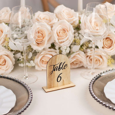Wooden table number sign "Table 6" with roses and glassware in elegant setting.