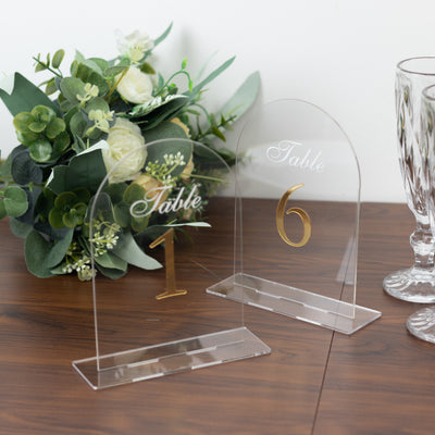 Acrylic table number signs with gold lettering on a wooden table.