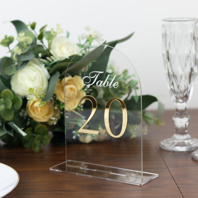 Acrylic table number sign with gold lettering, table 20, floral arrangement in background.