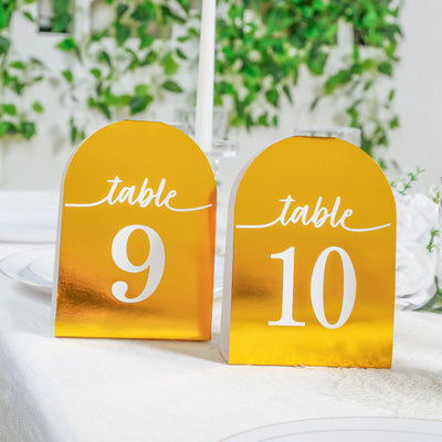 Gold table numbers 9 and 10 on a dining table with greenery backdrop.