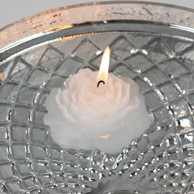 White rose-shaped candle floating in a decorative glass bowl.