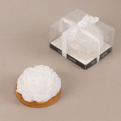 White flower-shaped candle with wooden base and clear gift box.