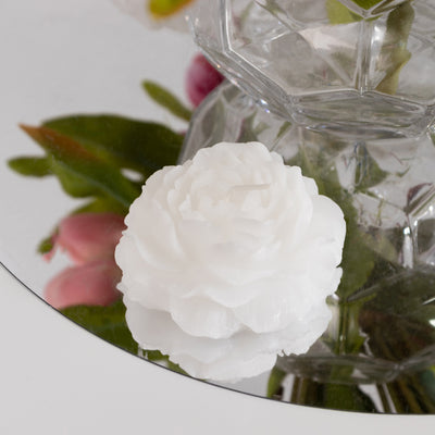 White floral candle with detailed petals on a mirrored surface.