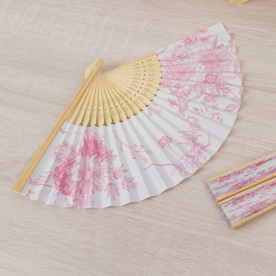 Pink floral folding fan with bamboo handle on a light wooden surface.
