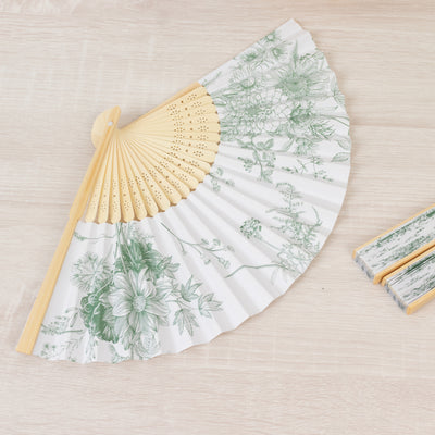 Floral design folding fan with bamboo handle on a wooden surface.