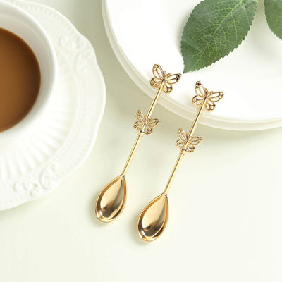 Gold butterfly spoons beside a cup of coffee and a plate.