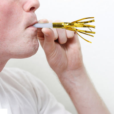 Person blowing into a party horn with gold streamers.