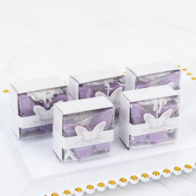 Butterfly-shaped soap bars in clear boxes on a marble surface.