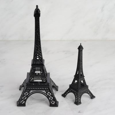 Black Eiffel Tower models in two sizes on a marble surface.