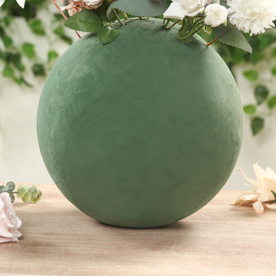 Green spherical vase with flowers on a wooden surface.