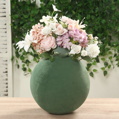 Green round vase with mixed floral arrangement on a wooden table.