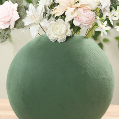 Green round vase with white and pink flowers on a wooden table.