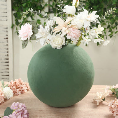 Green spherical vase with flowers arranged on a wooden table.