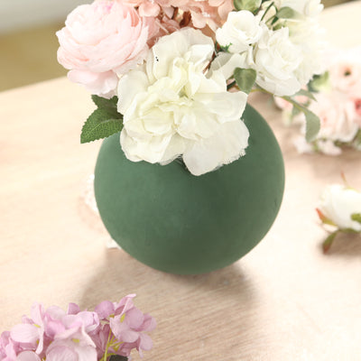 Green vase with artificial flowers on a wooden table.
