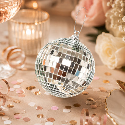 Silver disco ball ornament with rose gold confetti and candles on a festive table