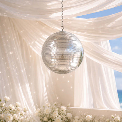 Elegant mirrored disco ball hanging under sheer drapes at a beach wedding venue