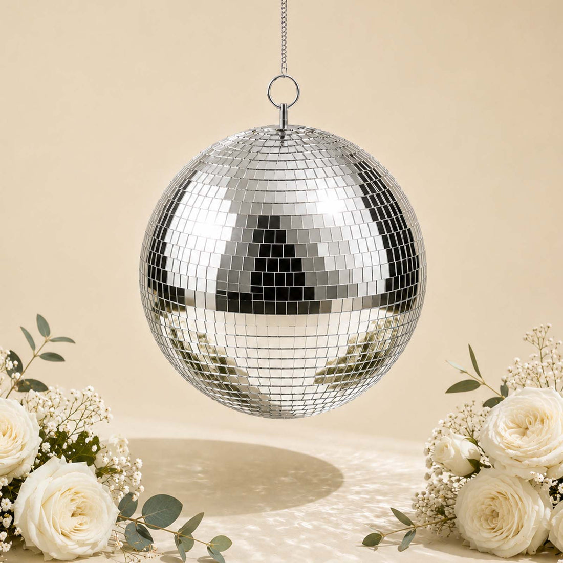 Silver mirrored disco ball hanging with white roses on a soft beige background