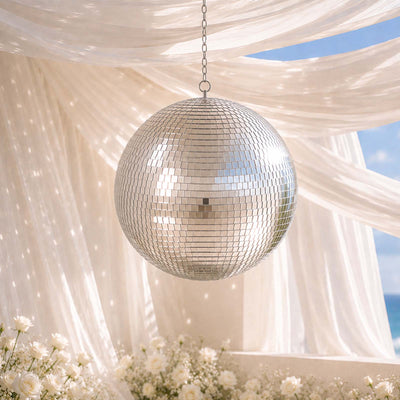 Silver disco ball hanging amid white drapes and flowers at an outdoor event