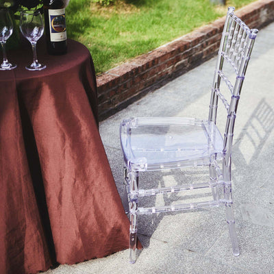 Clear acrylic chiavari chair beside a table with wine and glasses.