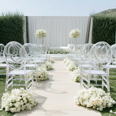 Elegant outdoor wedding setup with clear chairs and floral arrangements.