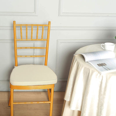 Gold chiavari chair with cream cushion beside a table and magazine.