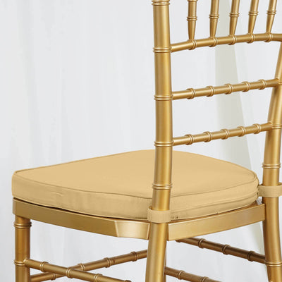 Gold chiavari chair with a beige cushion on a white backdrop.