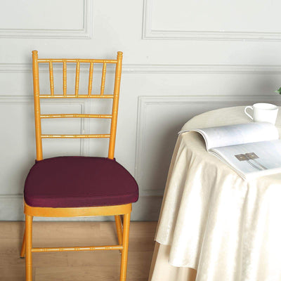 Gold chiavari chair with burgundy cushion beside a table.
