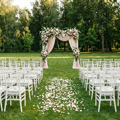 Outdoor wedding ceremony setup with floral arch and white chairs on a lawn