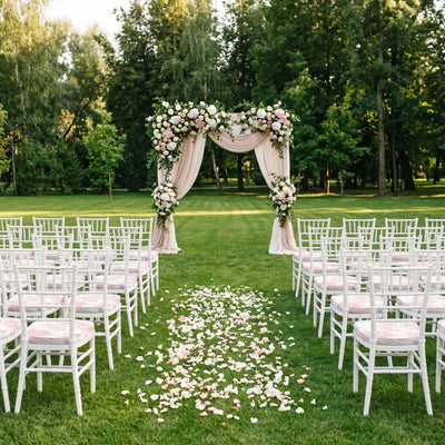 Outdoor wedding ceremony setup with floral arch, white chairs, and petal aisle