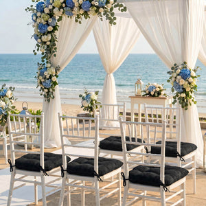 Beach wedding ceremony setup with floral arch and white chairs by the ocean