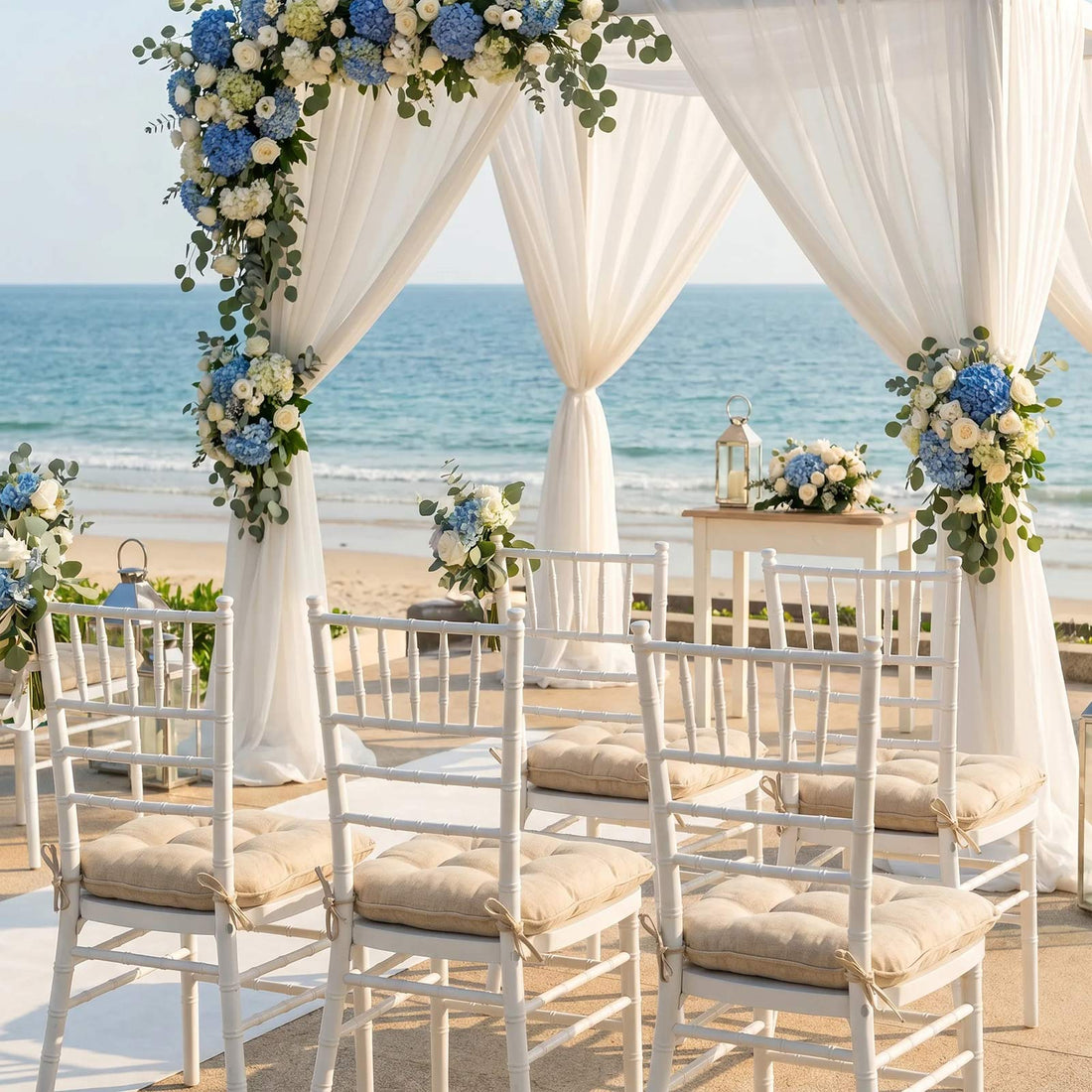Beach wedding ceremony setup with white drapes, blue floral arch, and ocean view