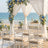 Beach wedding ceremony setup with white drapes, blue floral arch, and ocean view