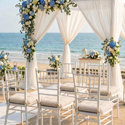 Beach wedding ceremony setup with floral arch, draped canopy, and white chairs