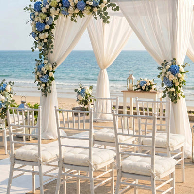 Beach wedding ceremony setup with white chairs, floral arch, and ocean backdrop