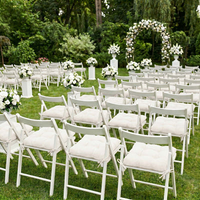 Outdoor wedding ceremony setup with white chairs and floral arch on a lawn