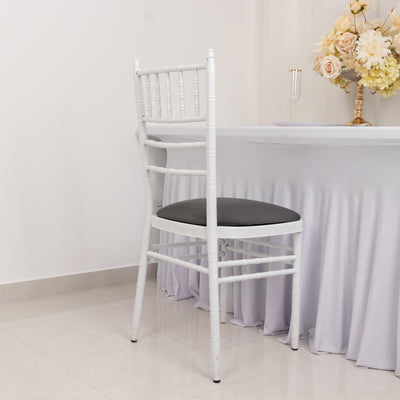 White chiavari chair with black cushion against a plain backdrop.