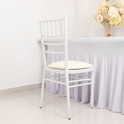 White chiavari chair with cream cushion beside a table draped in light fabric.