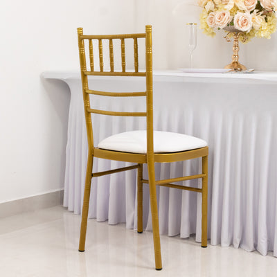 Gold chiavari chair with white cushion against a backdrop of a table and floral arrangement.