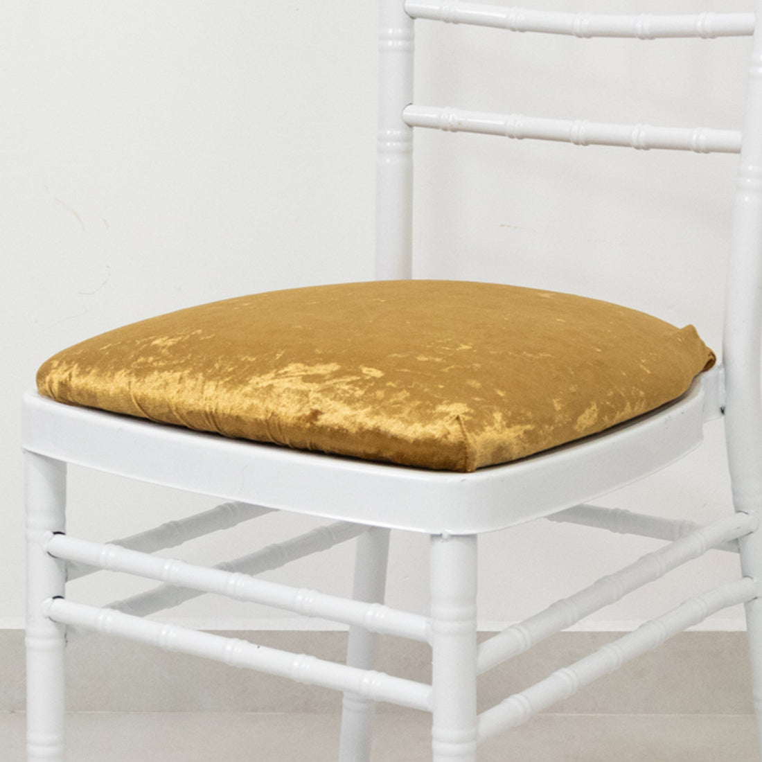 Gold velvet chair cushion on a white rustic chair.