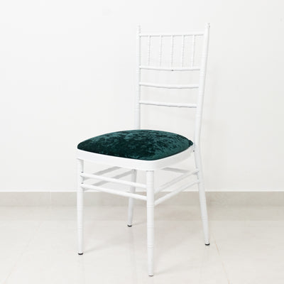 White chiavari chair with green velvet seat on a plain background